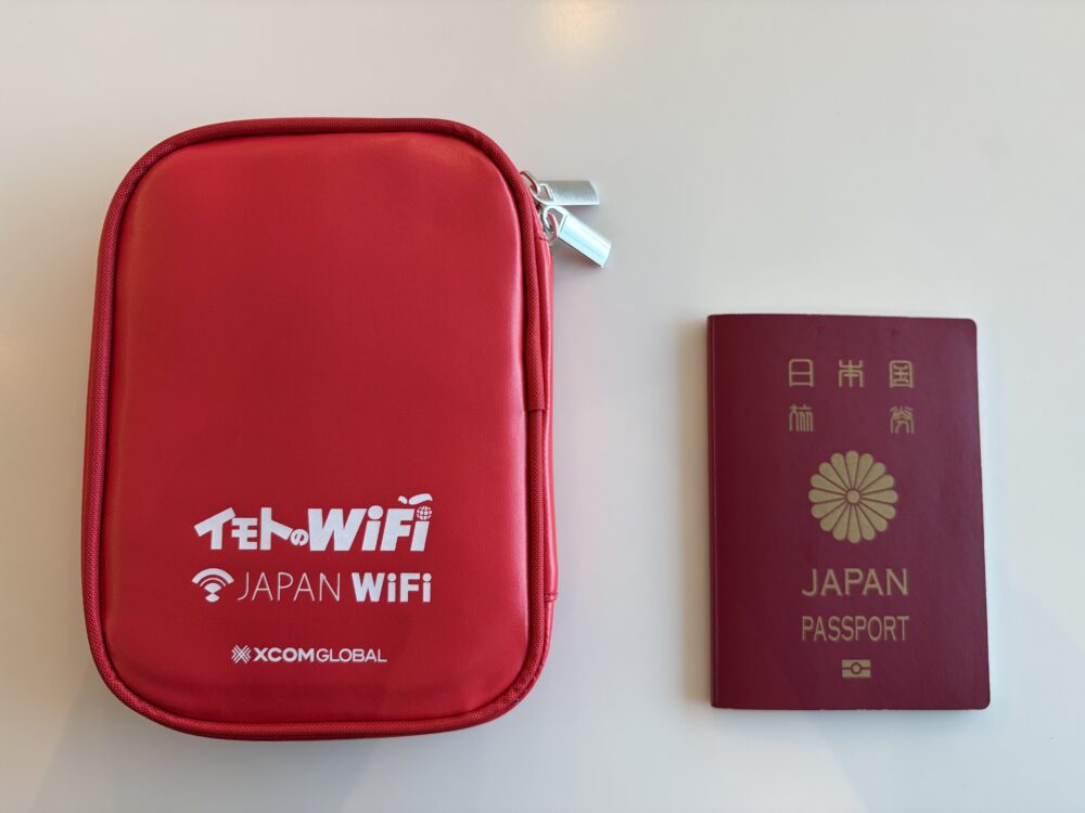日本のパスポートと並べたイモトのWiFiの赤い専用ポーチのサイズ比較