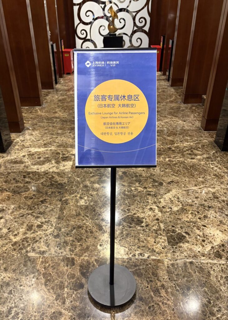 上海浦東国際空港V39ラウンジ内に設置されたスタンド看板。「旅客专属休息区（日本航空 大韓航空） Exclusive Lounge for Airline Passengers (Japan Airlines & Korean Air) 航空会社専用エリア（日本航空 ＆ 大韓航空）」と日英中韓の4ヶ国語で書かれている様子