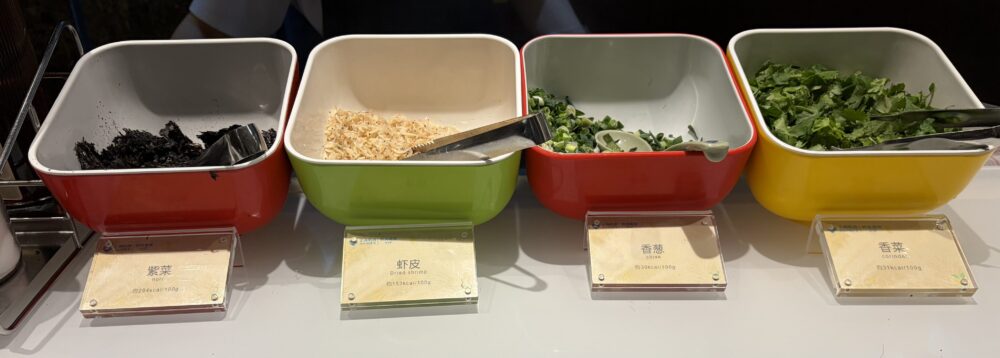 上海浦東国際空港V39ラウンジのヌードルバーに用意されているラーメン用の薬味・トッピング。左から海苔（紫菜）、干しエビ（蝦皮）、ネギ（香葱）、パクチー（香菜）がカラフルな器に並んでいる様子