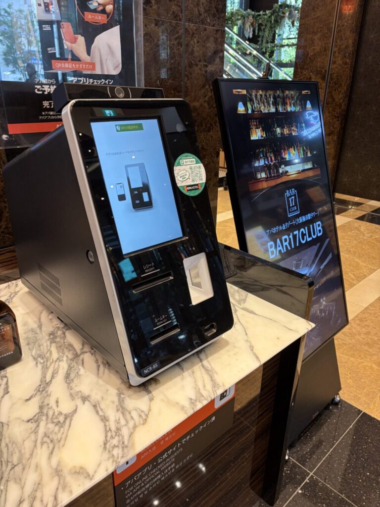 アパホテルのロビーに設置されている「1秒チェックイン」用の自動チェックイン機。画面にQRコードの読み取り案内が表示されている
