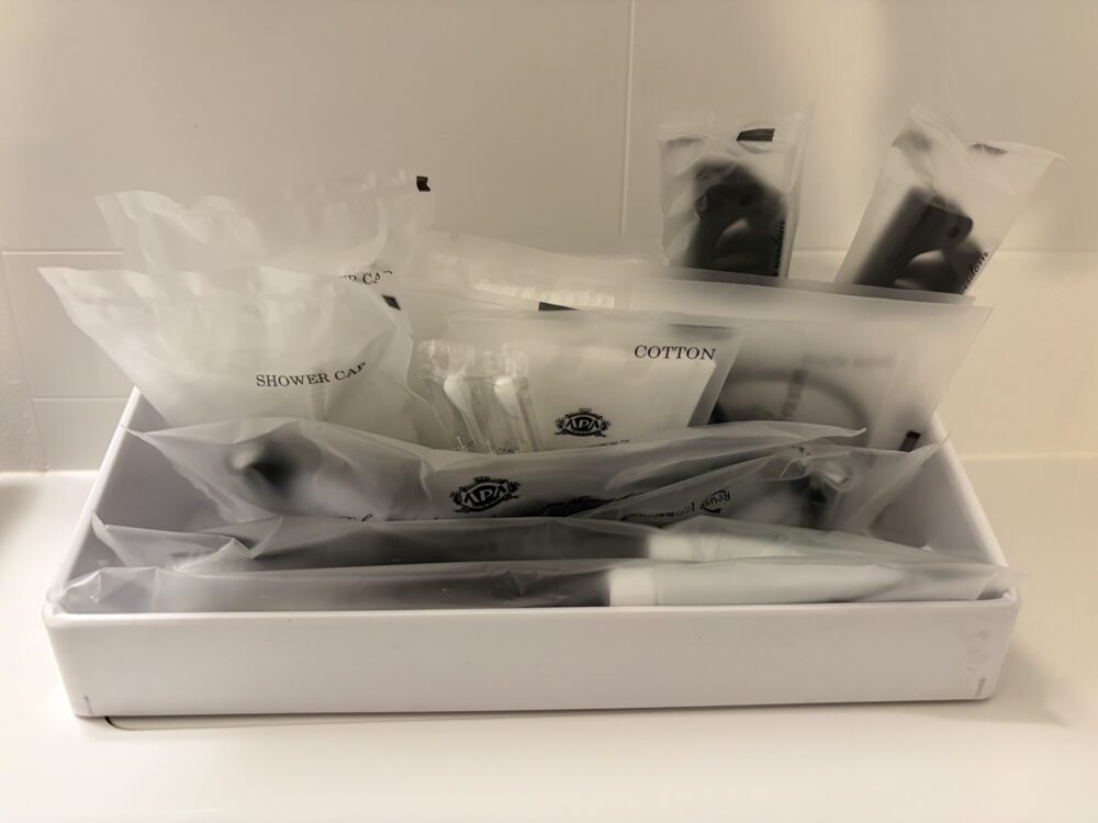 白のボックスに綺麗にまとめられたアパホテルの客室アメニティ一式。歯ブラシ、ひげ剃り、シャワーキャップ、コットンなどが並んでいる。